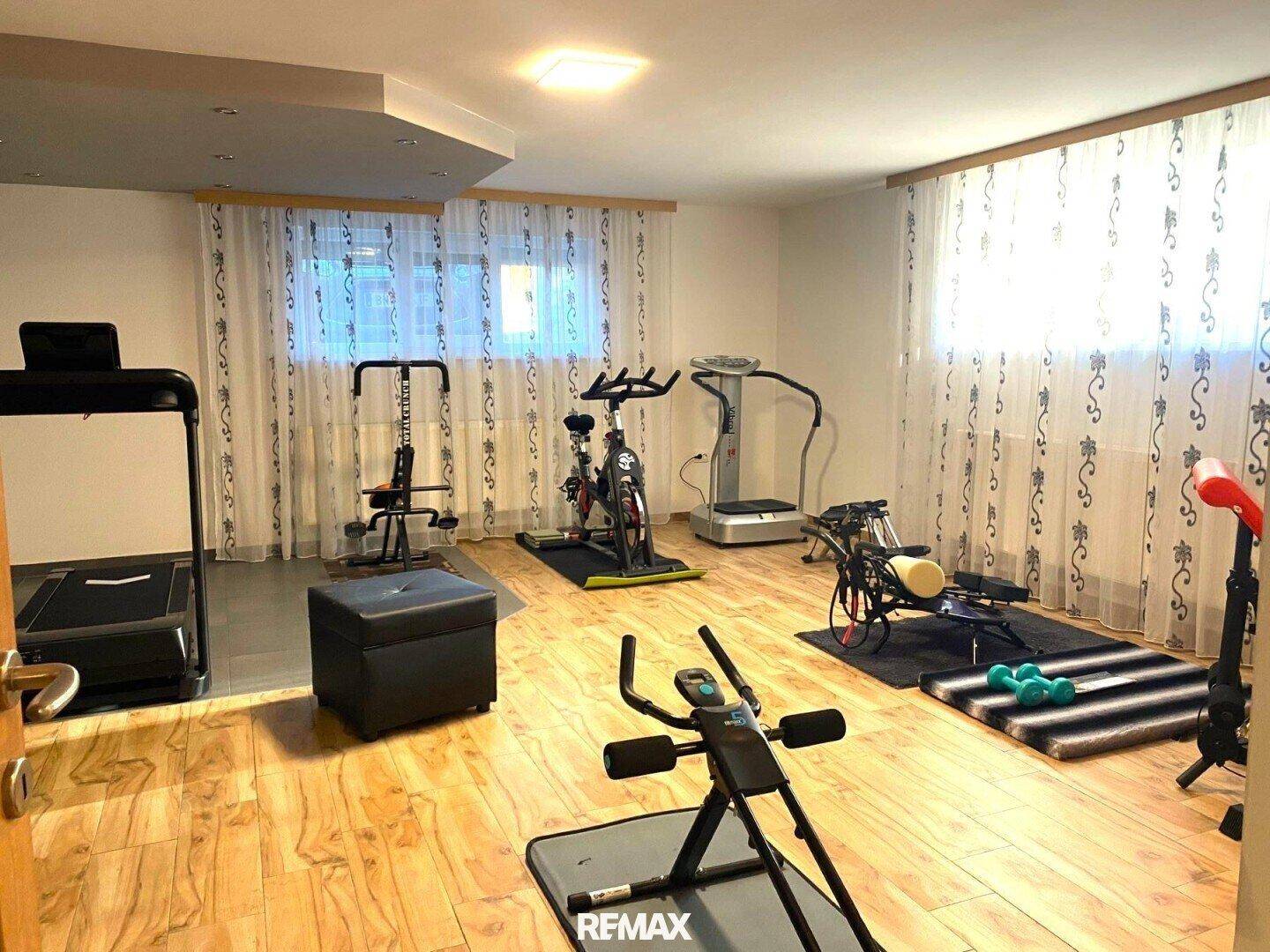 Geräumiger Fitnessraum mit verschiedenen Trainingsgeräten und hellem Holzfußboden, gut beleuchtet.