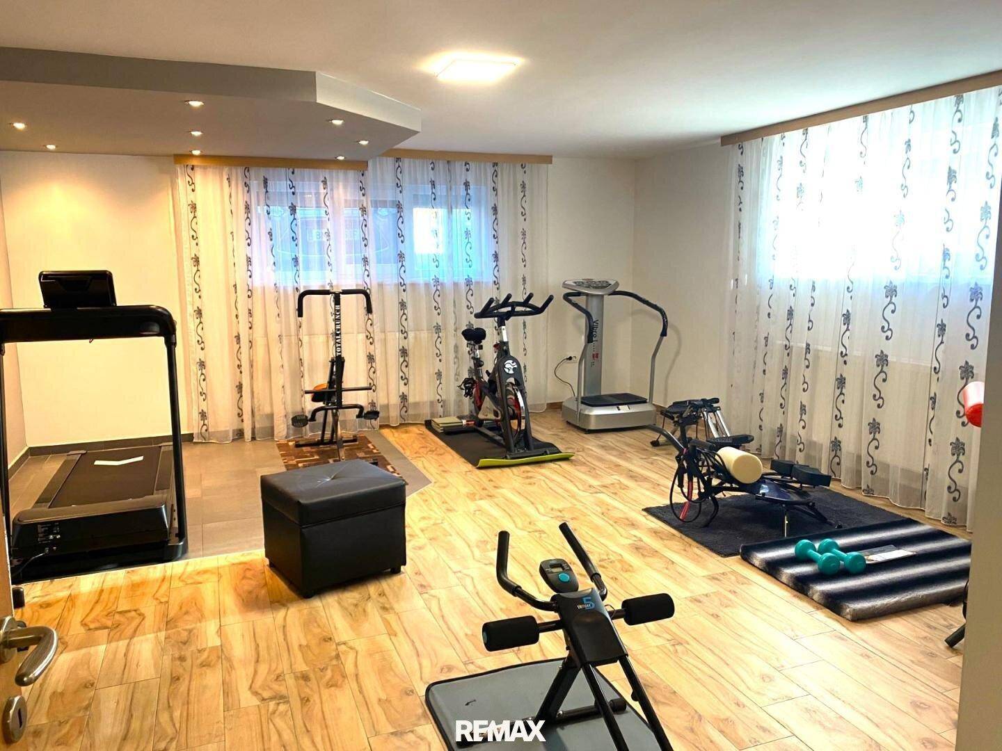 Geräumiger Fitnessraum mit verschiedenen Trainingsgeräten und hellem Holzfußboden, gut beleuchtet.
