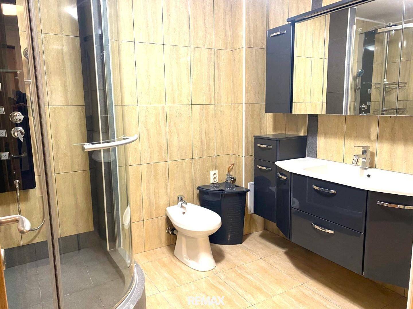 Badezimmer mit Duschkabine, Bidet und modernem Waschtisch, komplett gefliest in warmen Farbtönen.