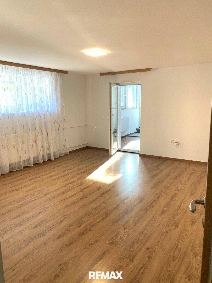 Helles Zimmer mit Holzfußboden und Zugang zu einem weiteren Raum, gut beleuchtet.