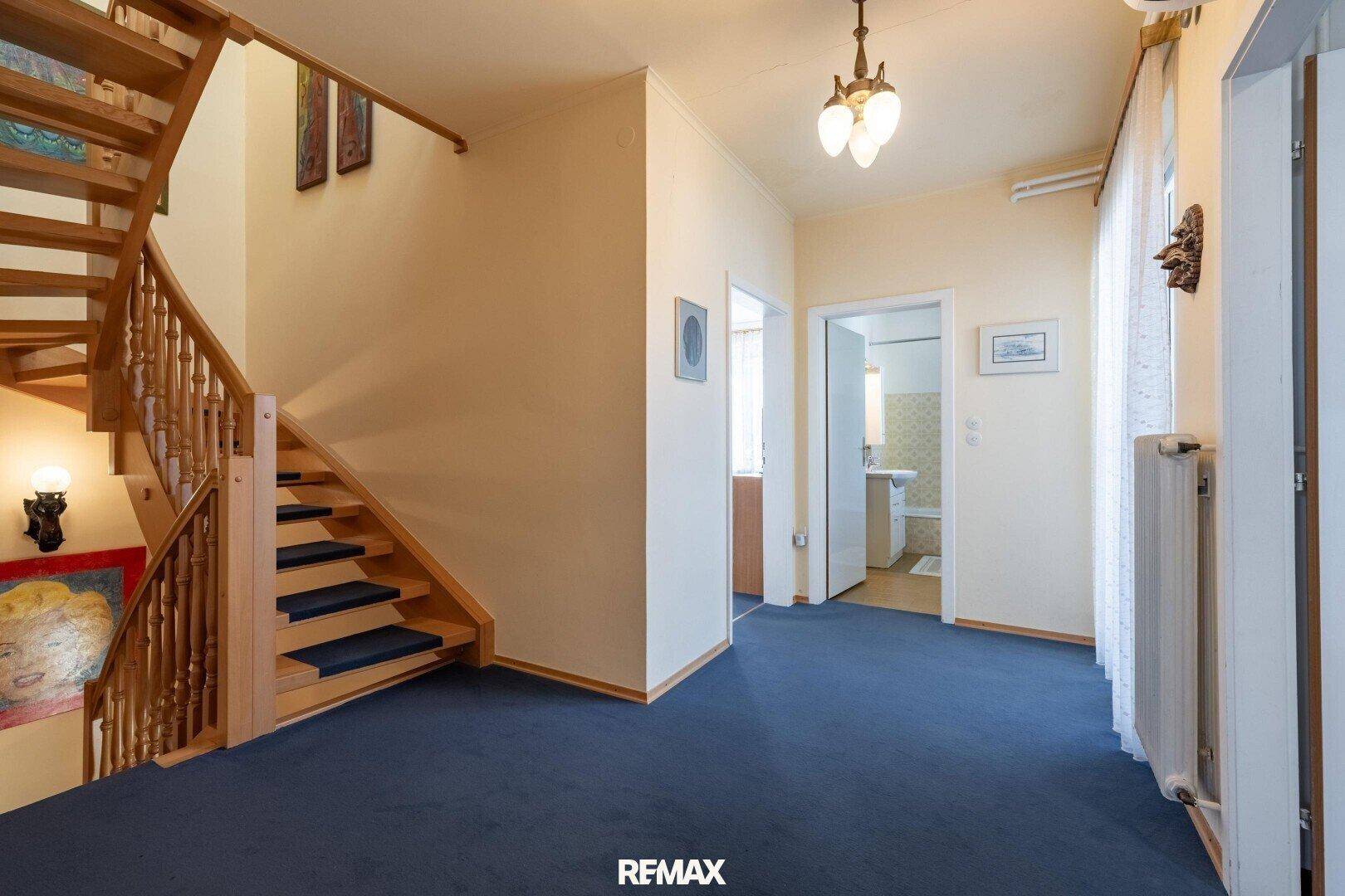 Geräumiger Flur mit Holztreppe, Teppichboden und Zugang zu weiteren Räumen.