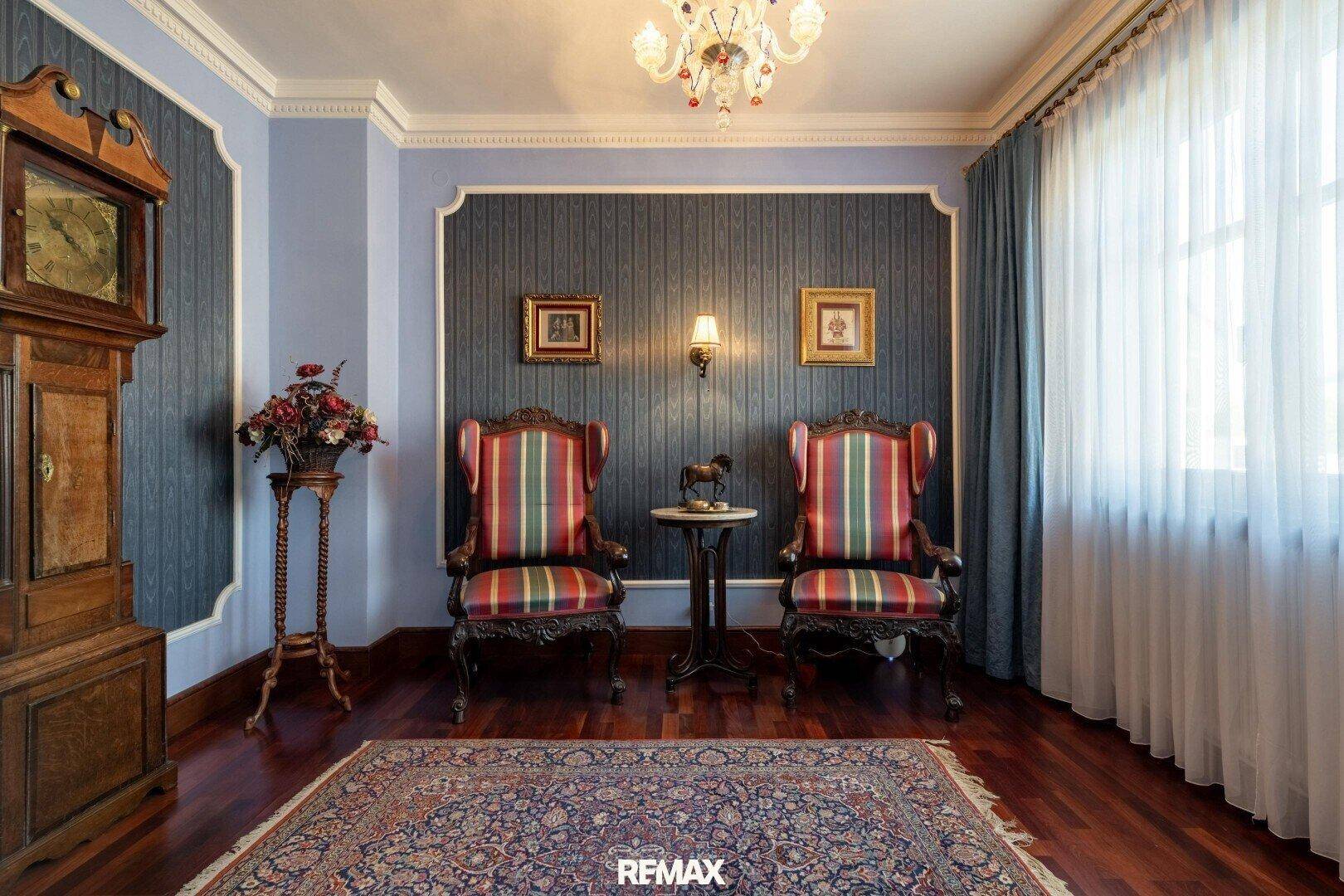 Elegantes Wohnzimmer mit blauen Wänden, antiken Sesseln und einem großen Fenster.