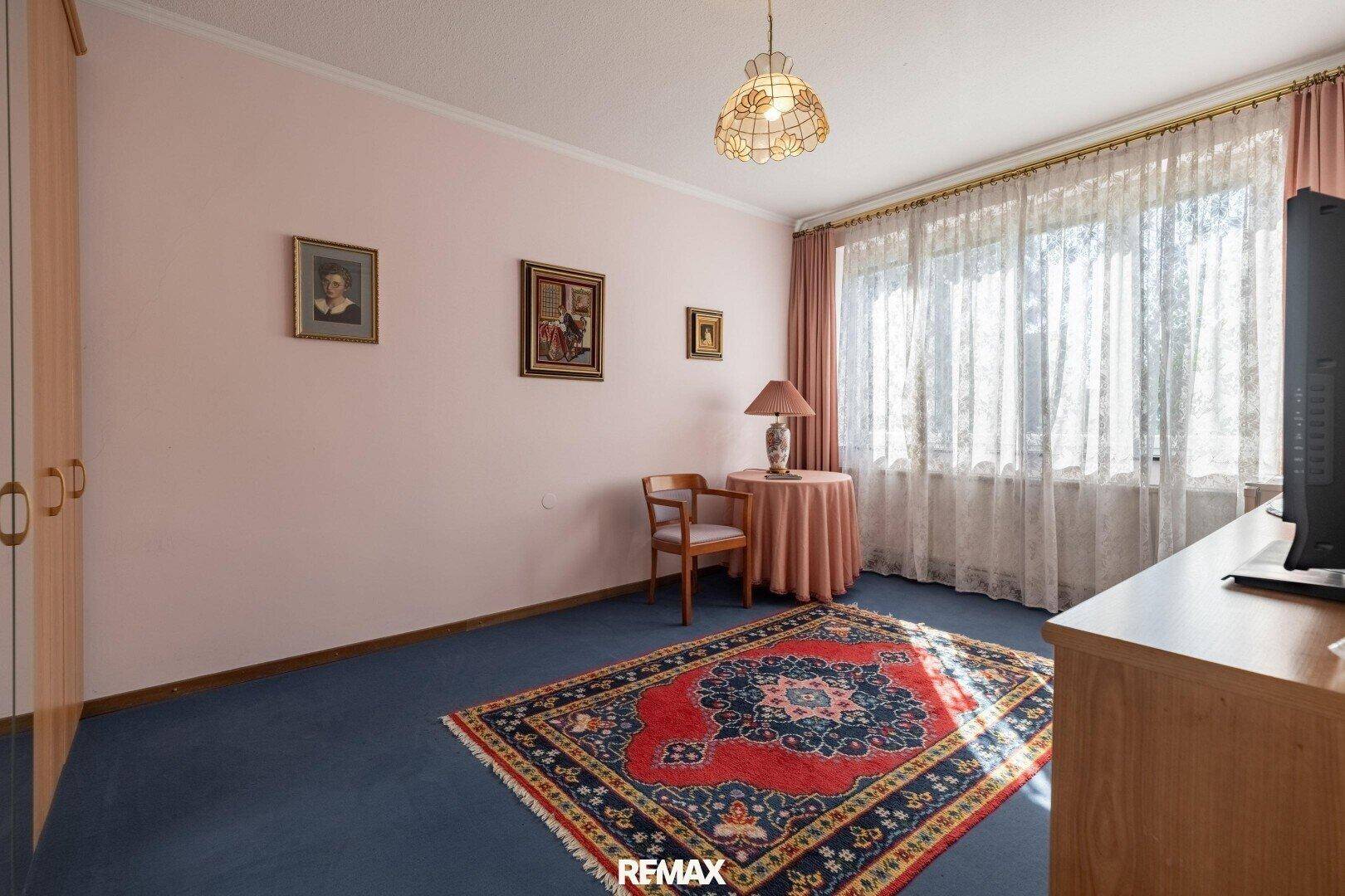 Helles Schlafzimmer mit blauem Teppichboden, großem Fenster und traditioneller Einrichtung.