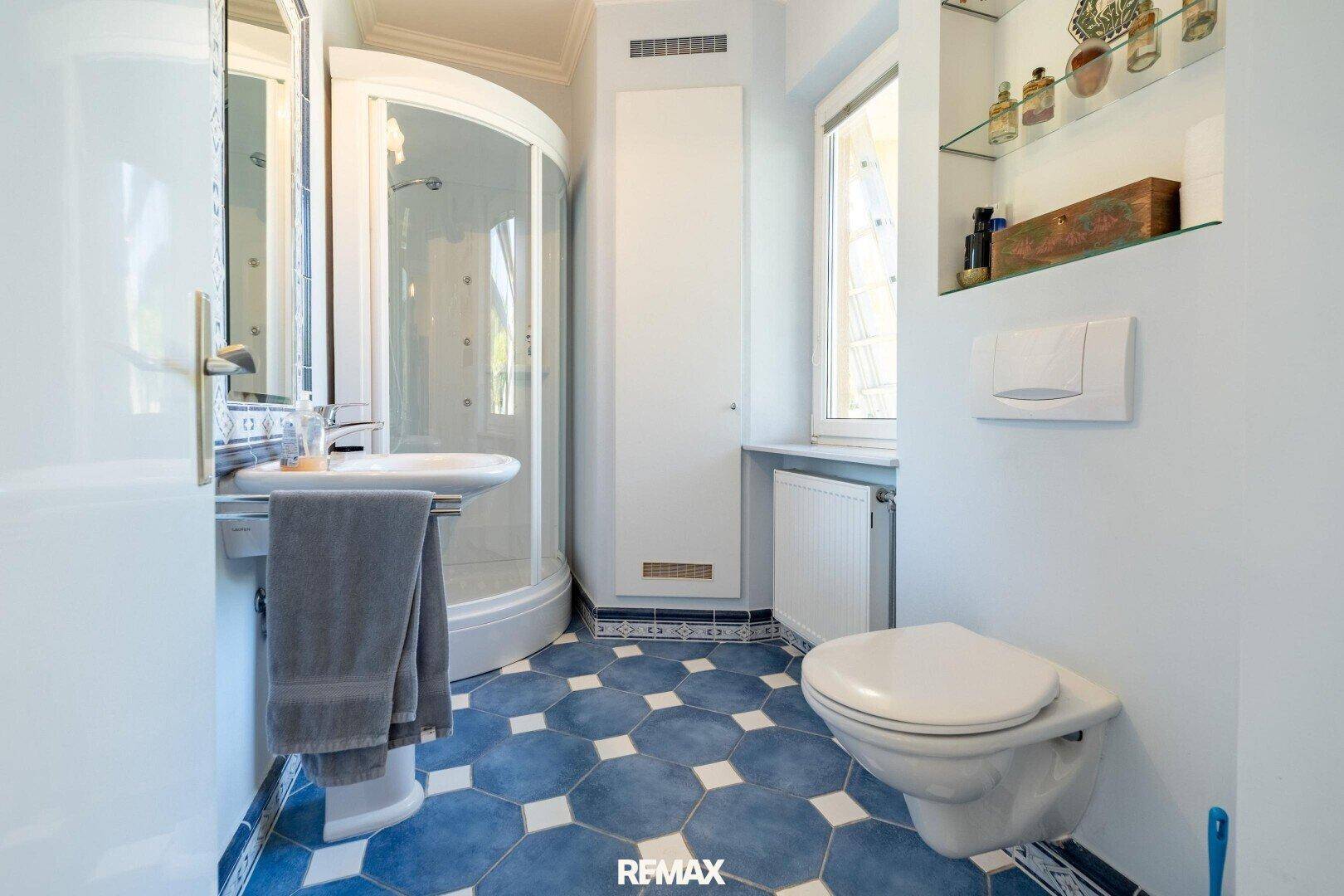 Modernes Badezimmer mit blauen Fliesen, Duschkabine und wandhängendem WC.