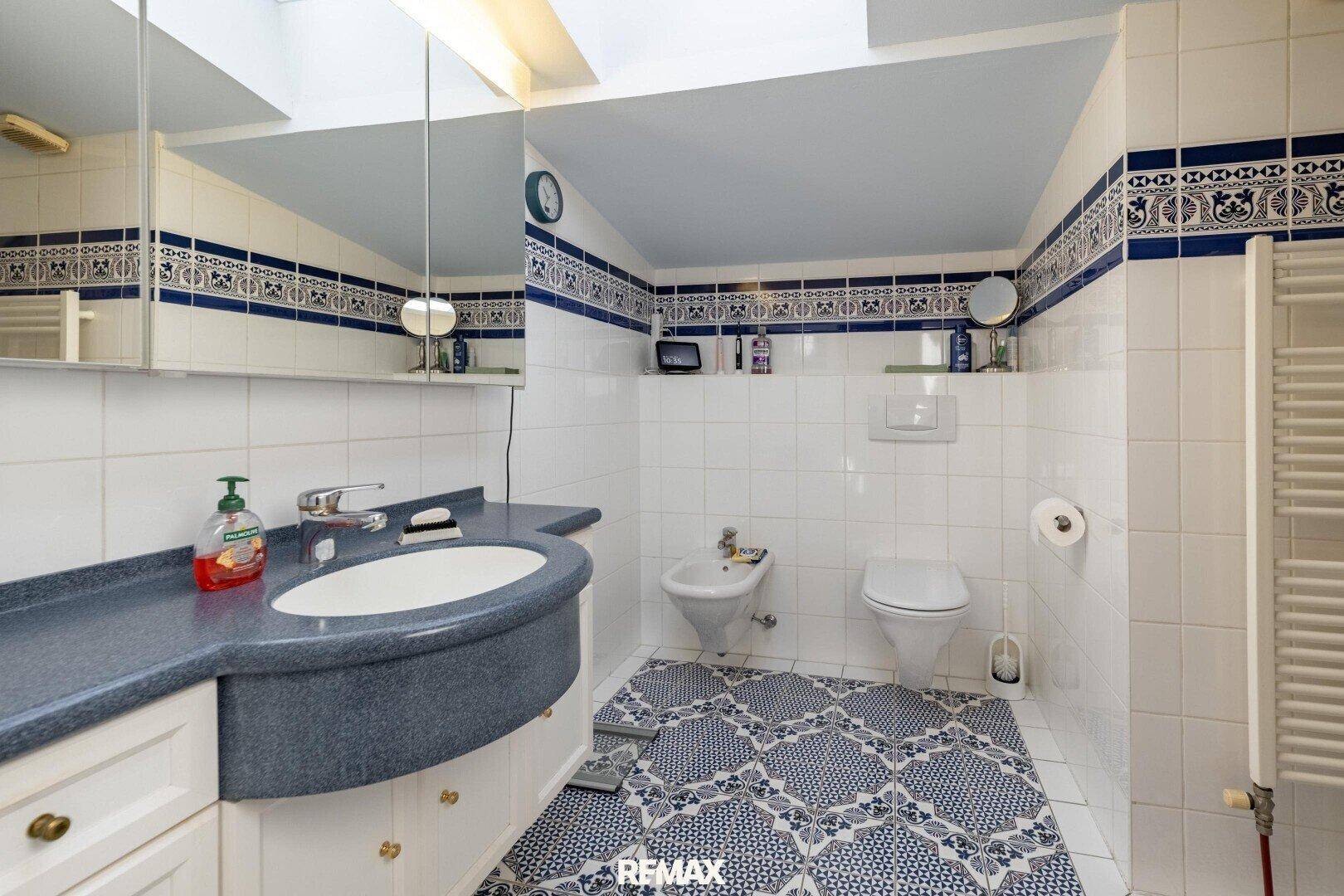 Badezimmer mit Waschbecken, Spiegelschrank, WC und Bidet, dekoriert mit blauen Fliesen.