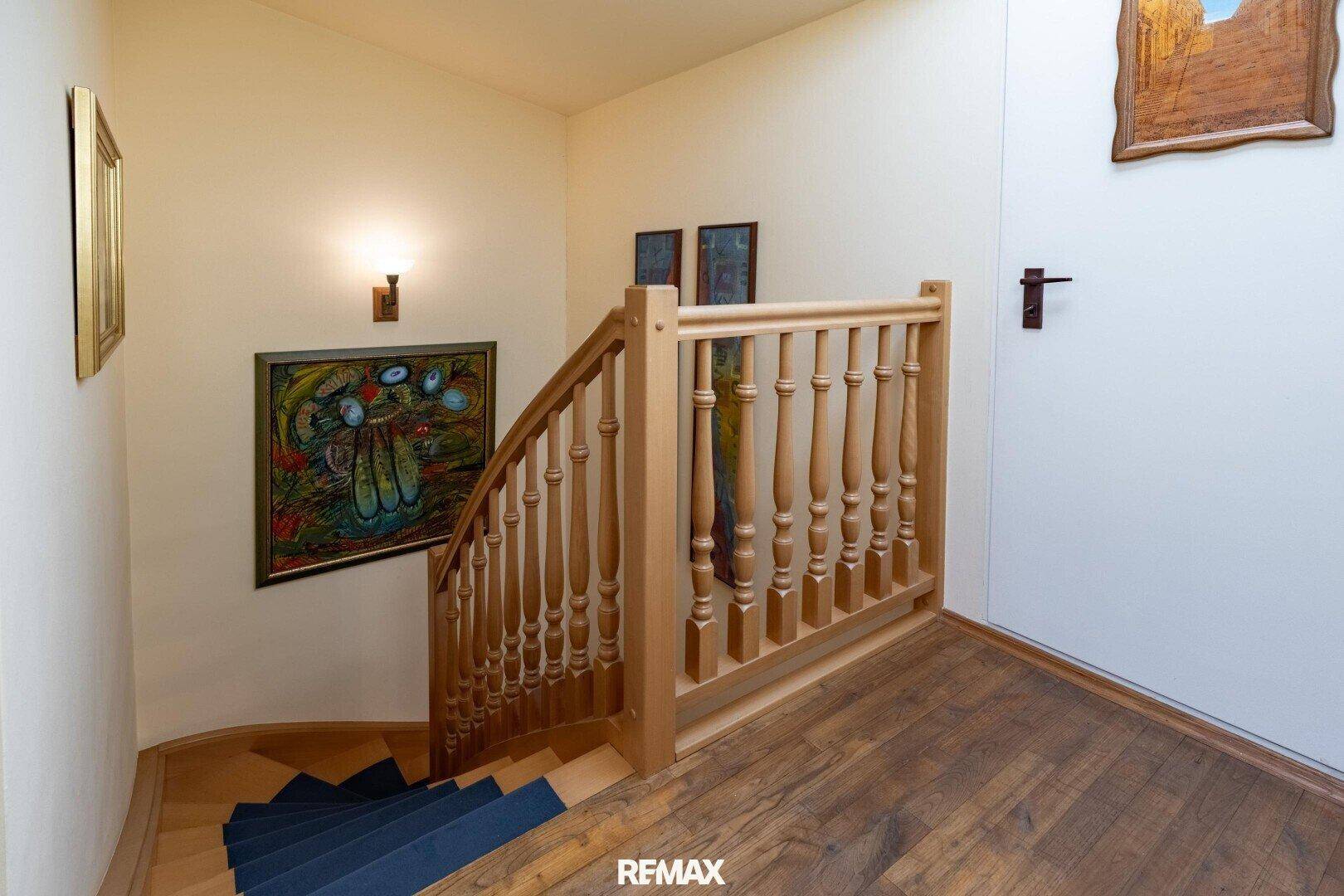 Holztreppe mit Geländer in einem hellen Flur, der in die obere Etage führt.