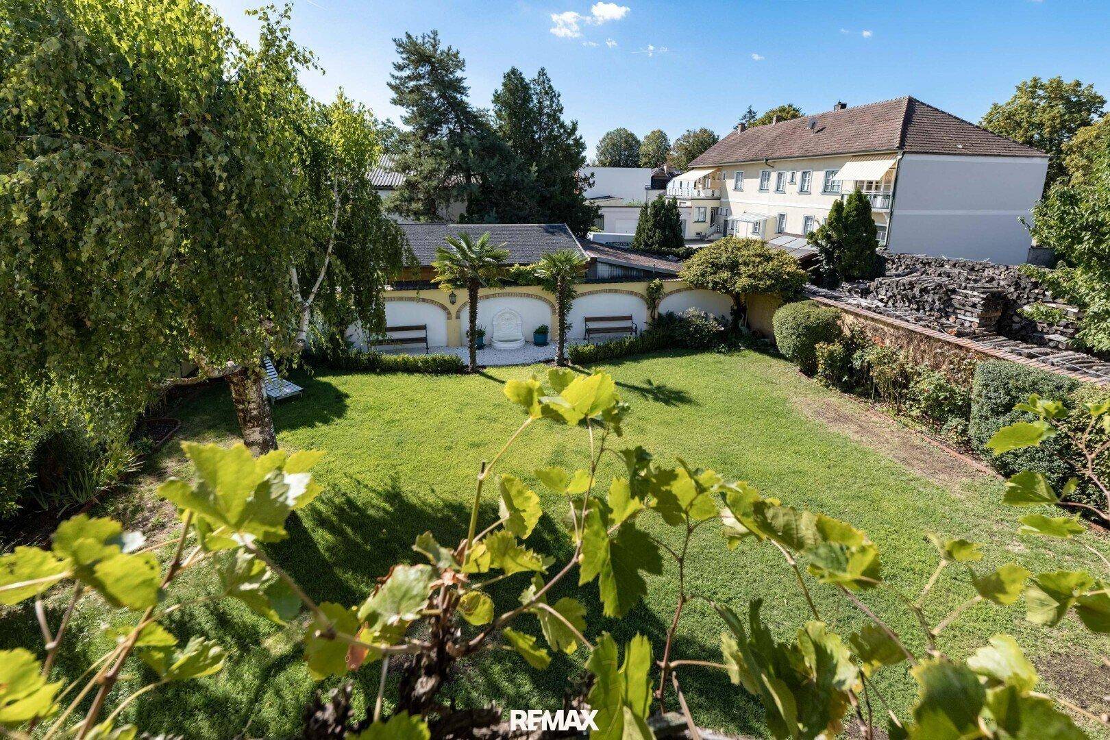 Weitläufiger Gartenbereich mit Rasen, Bäumen und Blick auf die umliegenden Gebäude.