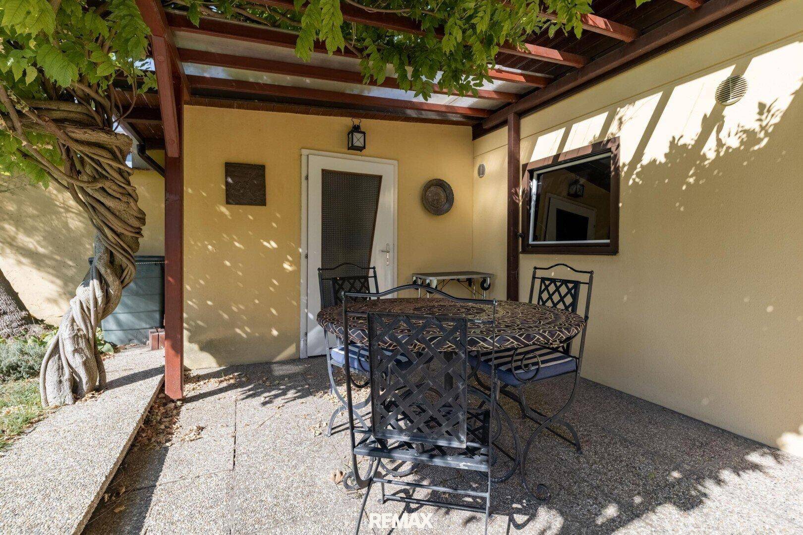 Überdachte Terrasse mit schmiedeeisernen Gartenmöbeln und Blick in den Garten.