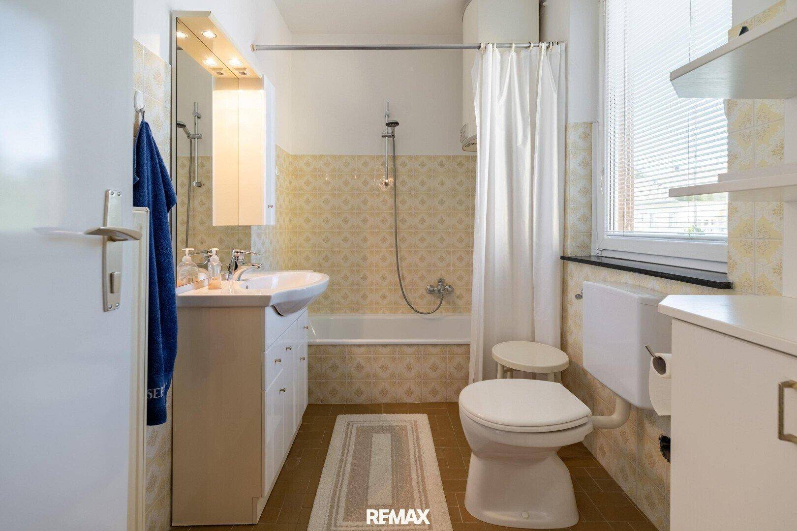 Badezimmer mit Badewanne, Duschvorhang, Waschbecken und Fenster.