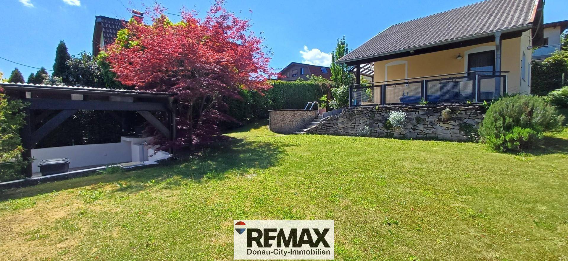 Großer grüner Garten mit Rasenfläche, Bäumen und einem überdachten Bereich neben dem Haus.