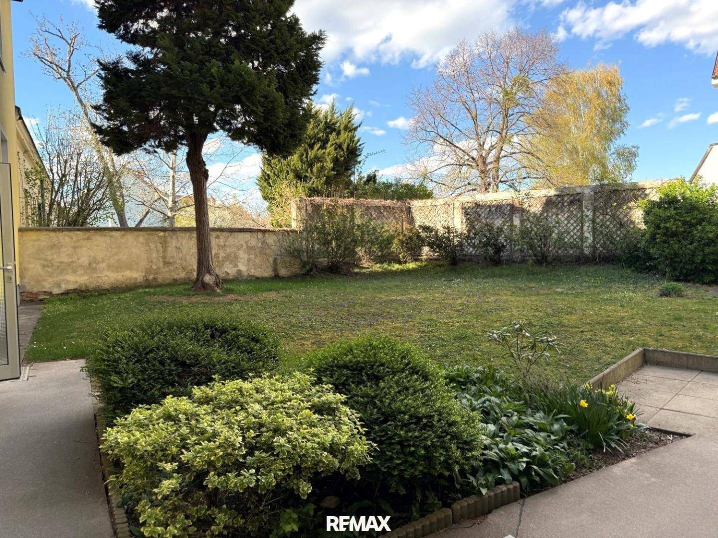 Großer, gepflegter Gartenbereich mit Rasenfläche, Sträuchern und einer kleinen Terrasse am Gebäude.