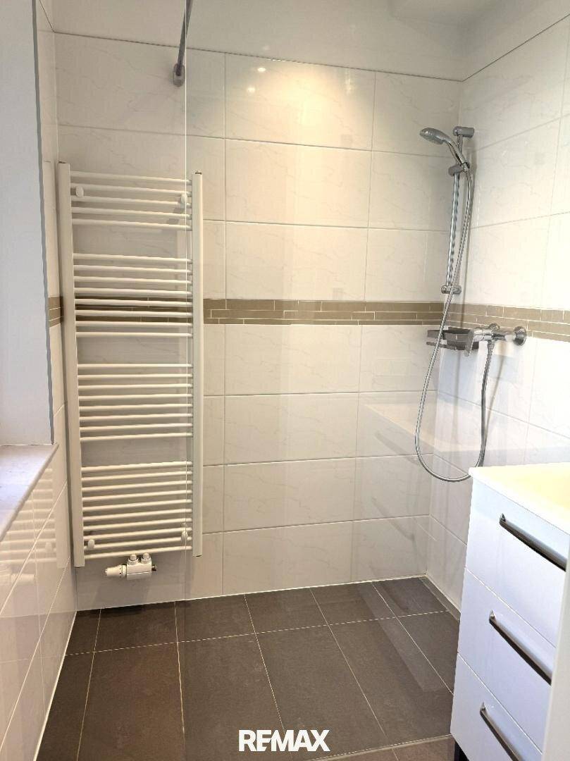 Modernes Badezimmer mit begehbarer Dusche, weißen und grauen Fliesen und beheiztem Handtuchhalter.