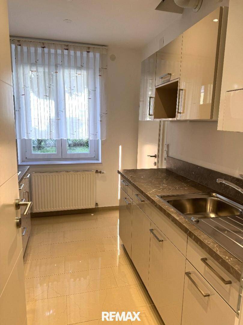 Funktionale Küche mit hellen Schränken, Spülbecken und Fenster, das viel Tageslicht hereinlässt.