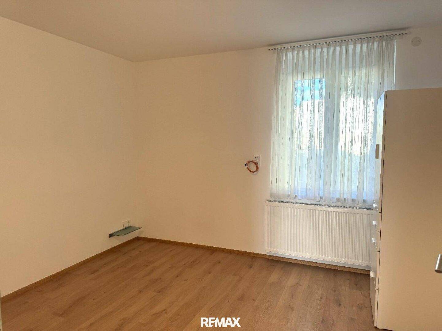 Helles Schlafzimmer mit Holzboden, weißen Wänden und einem Fenster mit Blick ins Grüne.