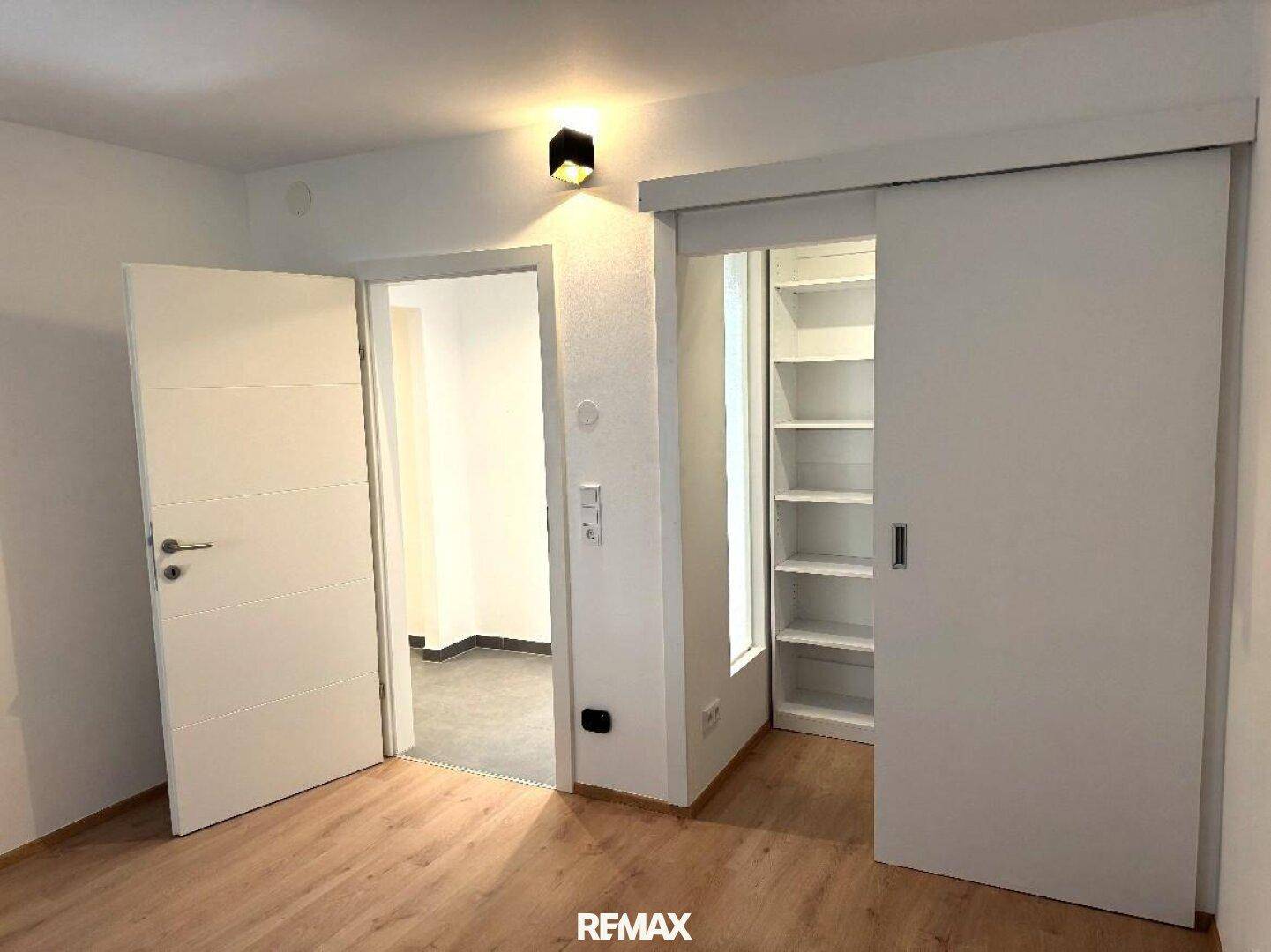 Heller Raum mit Holzboden, weißen Türen und einer Schiebetür, die einen begehbaren Kleiderschrank freigibt.
