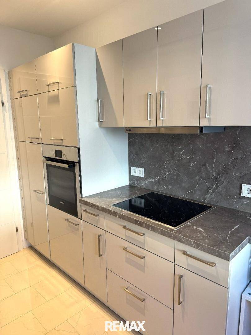 Moderne Einbauküche mit glänzenden Fronten, Induktionskochfeld und integriertem Backofen.