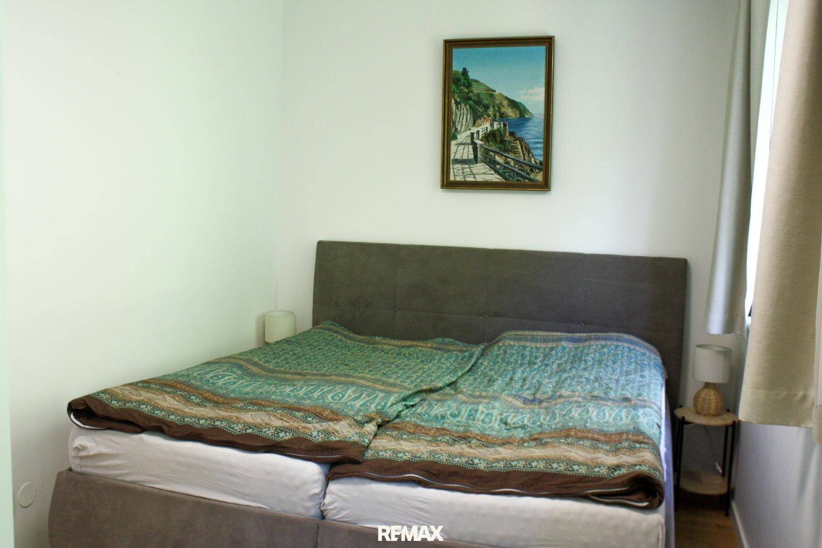 Schlafzimmer mit Doppelbett und einem Wandbild, das eine Küstenlandschaft zeigt.