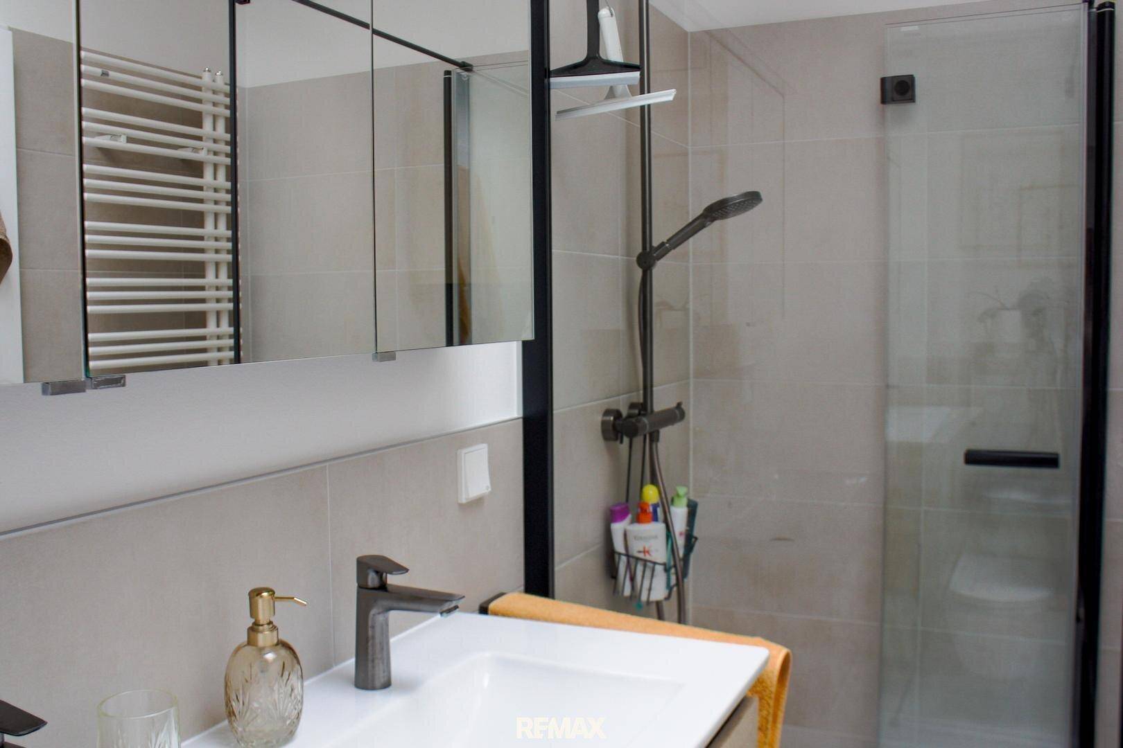 Modernes Badezimmer mit Waschtisch, Spiegelschrank, Duschkabine und Handtuchheizkörper.