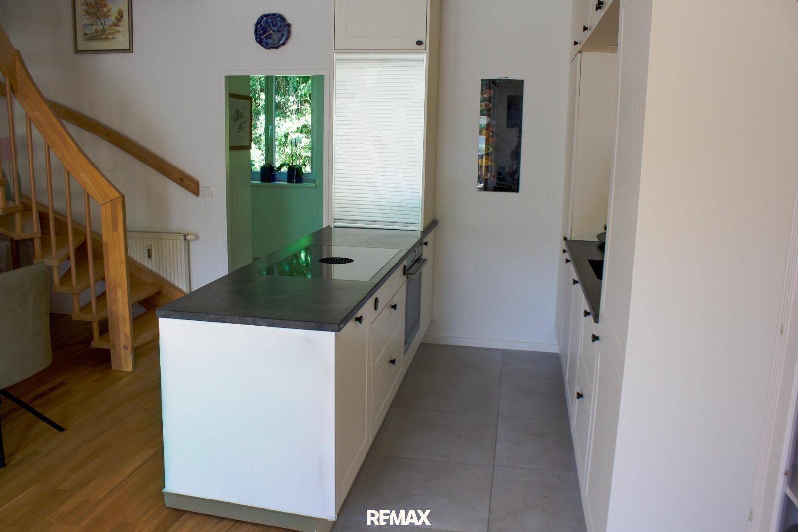 Funktionale Küche mit weißen Schränken, dunkler Arbeitsplatte und angrenzender Holztreppe.