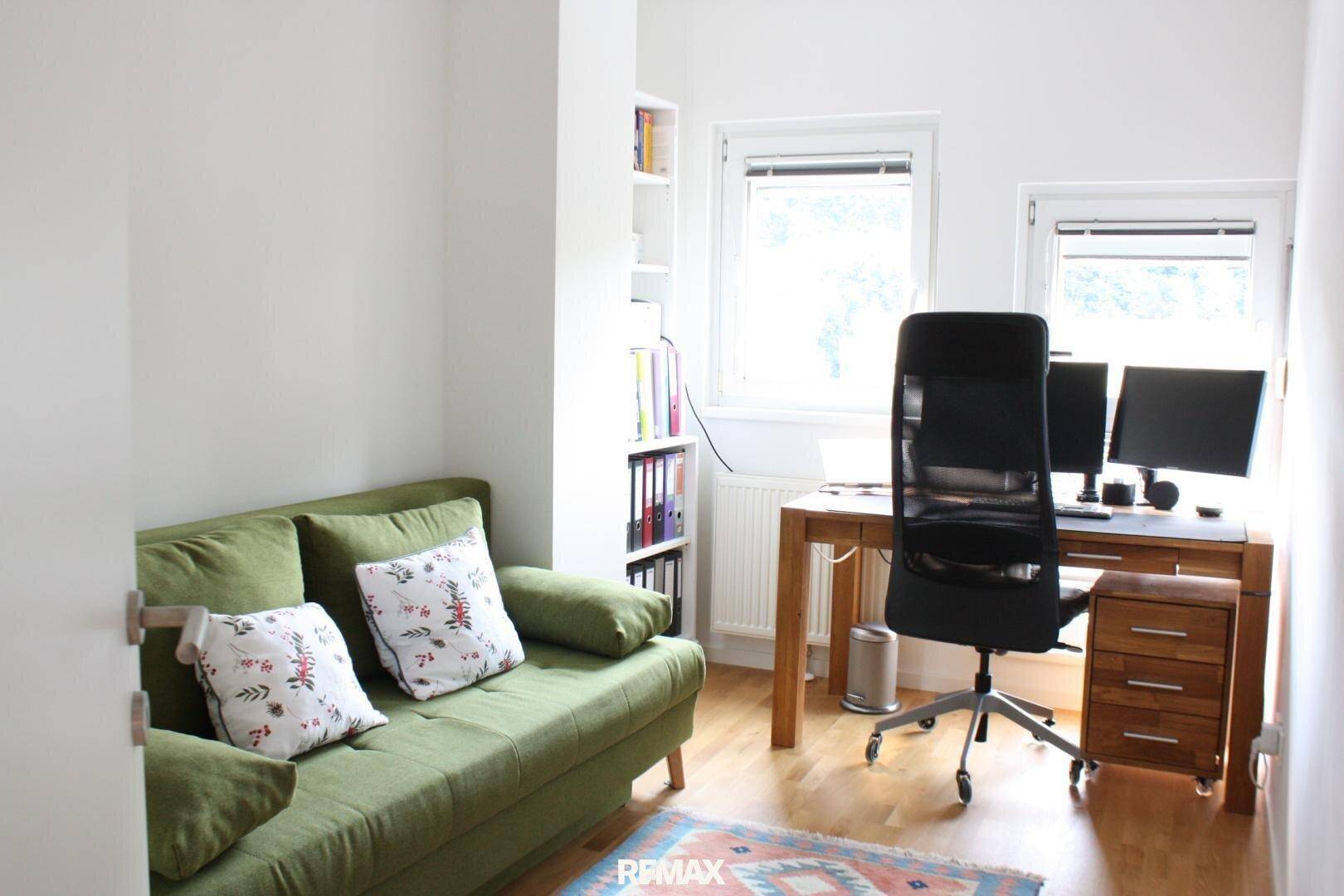 Helles Arbeitszimmer mit Schreibtisch, Bürostuhl und einem bequemen grünen Sofa.