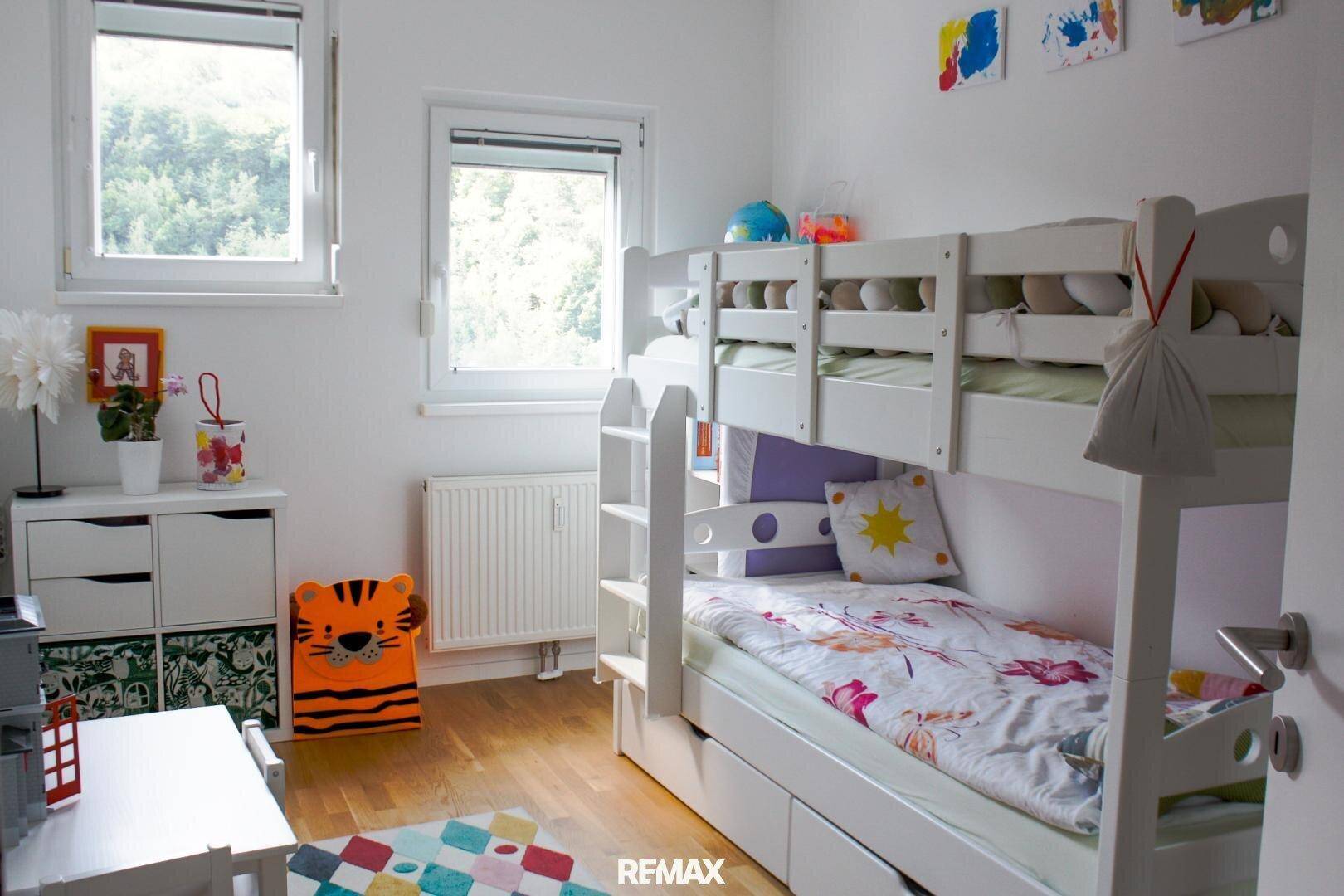 Freundliches Kinderzimmer mit Etagenbett, weißen Möbeln und bunten Akzenten.