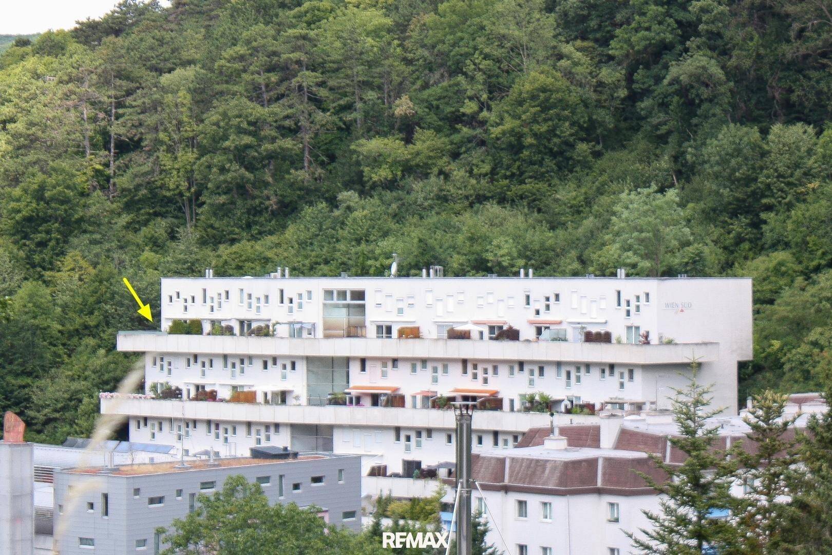 Mehrstöckiges Gebäude mit Balkonen, eingebettet in eine grüne Hügellandschaft.