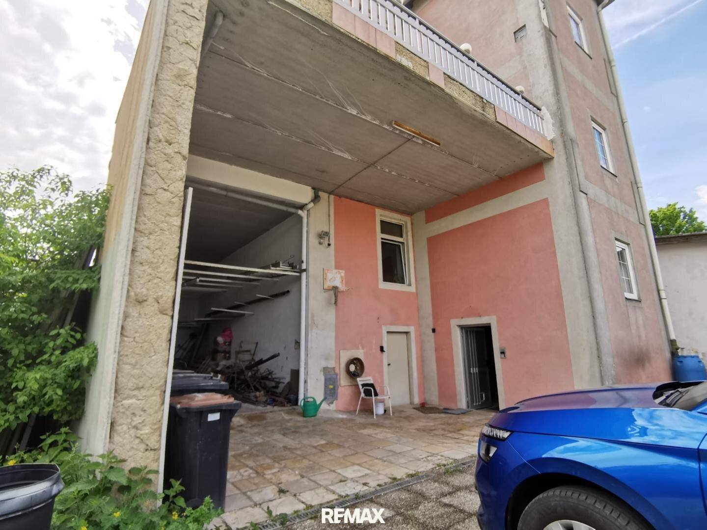 Außenansicht des Gebäudes mit großer Garageneinfahrt und rosa gestrichener Fassade.