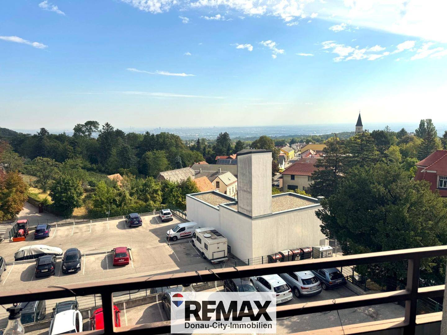 Balkon mit Blick auf einen Parkplatz, umliegende Gebäude und die weite Landschaft.