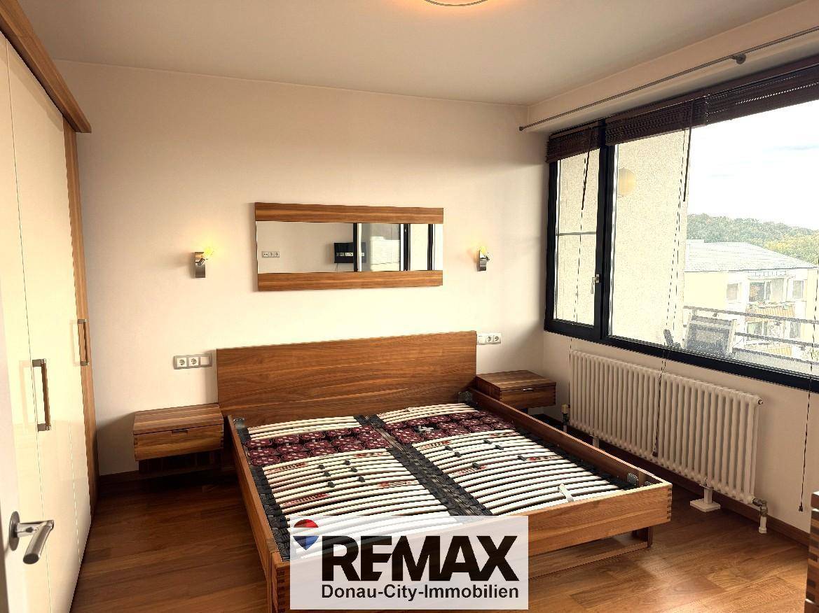 Helles Schlafzimmer mit Holzbett, Einbauschränken und einem Fenster mit Heizkörper.
