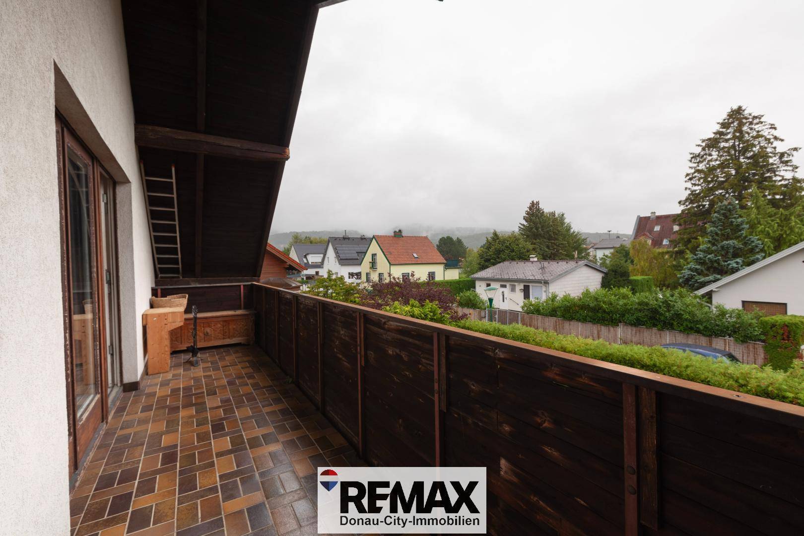 Großer Balkon mit Fliesenboden und Holzgeländer, bietet weite Aussicht auf die Umgebung.