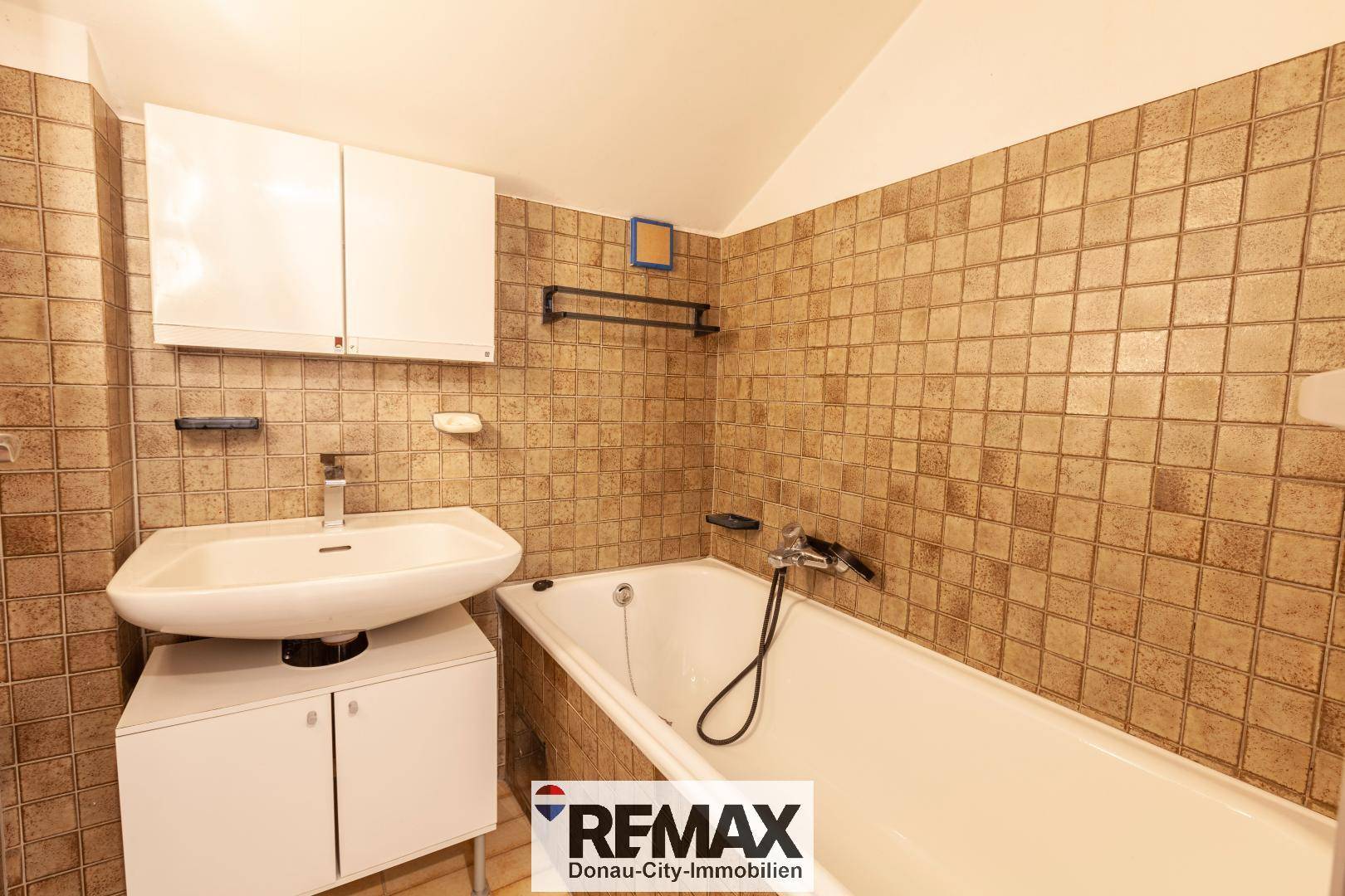 Badezimmer im 80er-Jahre-Stil mit braunen Fliesen, Badewanne und Einzelwaschbecken.