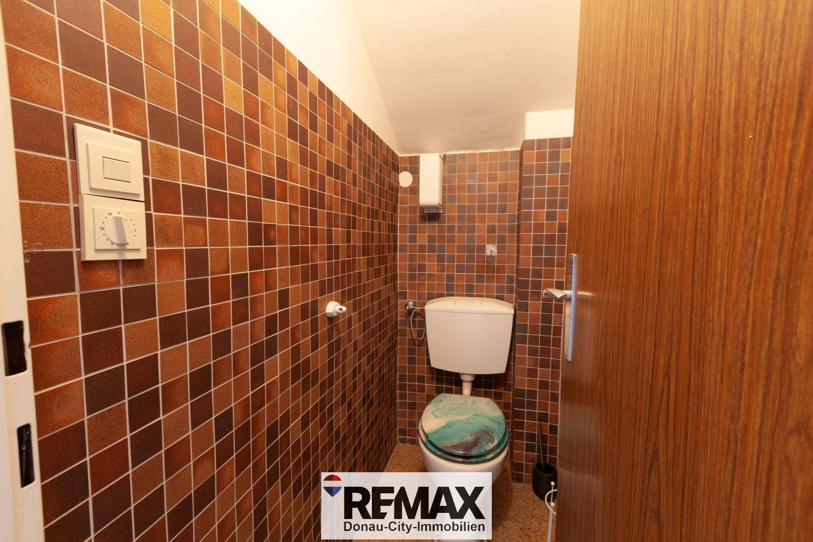 Separate Toilette mit braunen Fliesen an Wänden und Boden, sowie einem WC.
