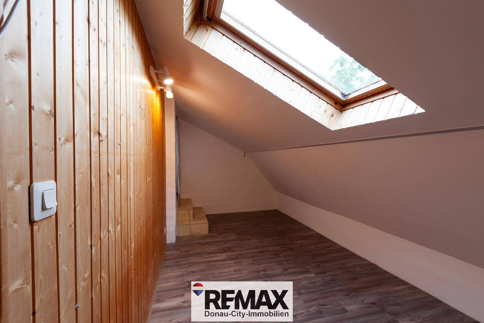 Dachbodenbereich mit Holzvertäfelung, Laminatboden und einem Dachfenster für Tageslicht.