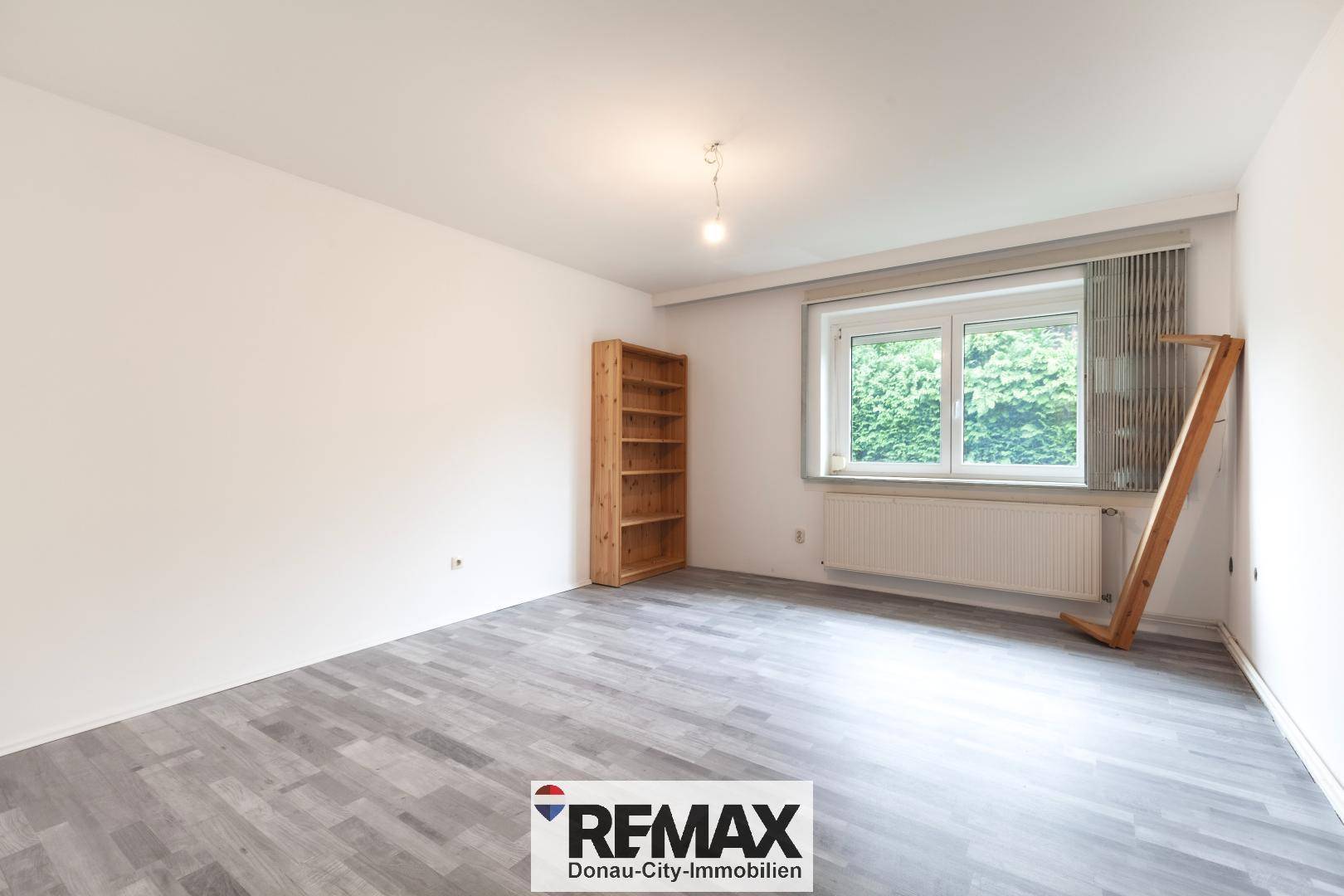 Geräumiges Zimmer mit Laminatboden, einem Holzregal und Blick ins Grüne.