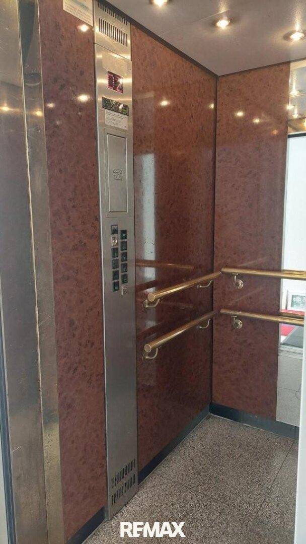 Moderner Aufzug mit braunen Marmorwänden und Haltegriffen im Gebäude.