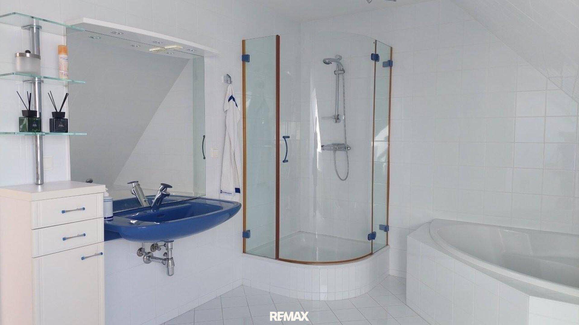 Weiß gefliestes Badezimmer mit Dusche, Badewanne und blauem Waschbecken unter Dachschräge.