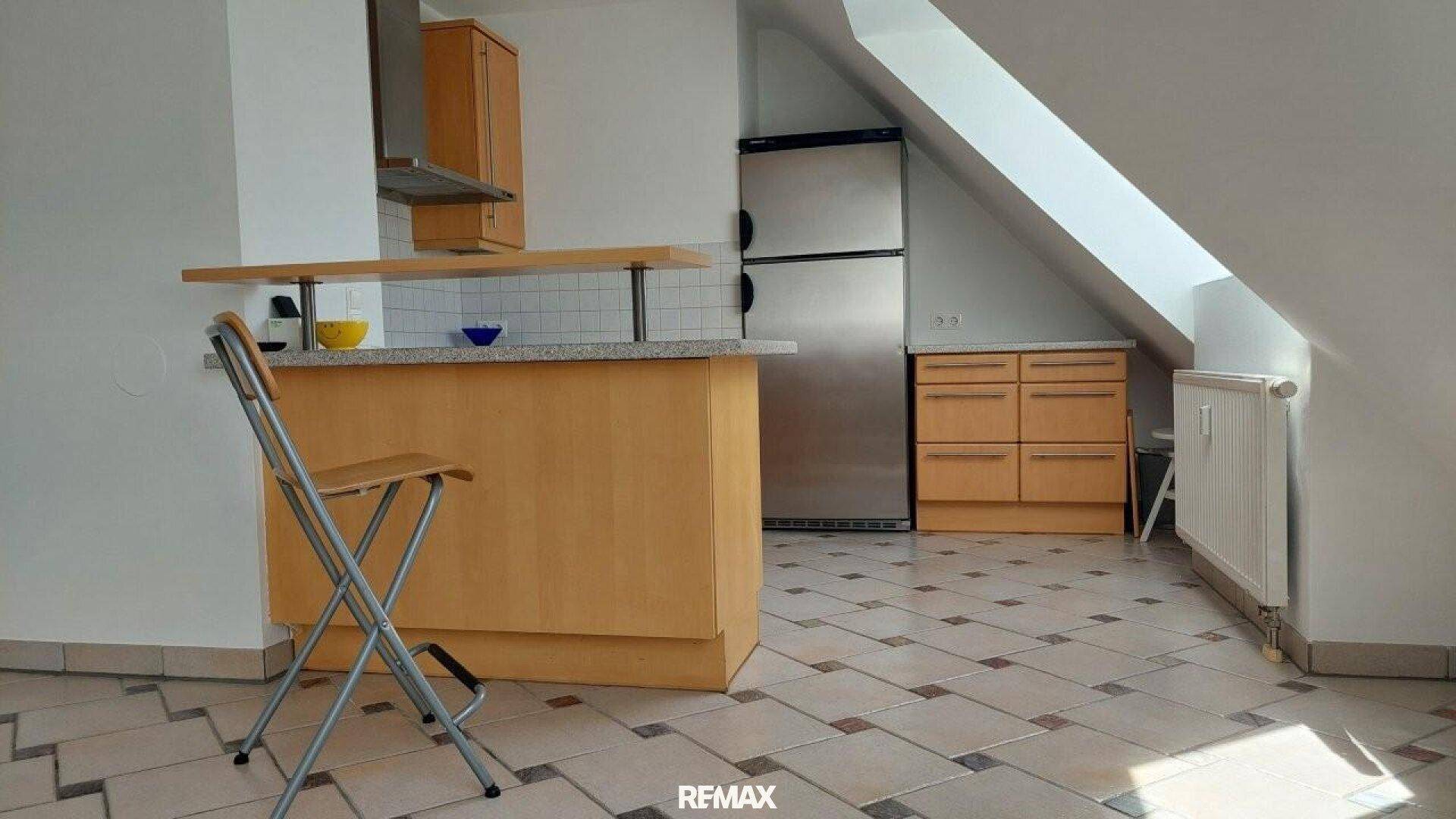 Offene Küche mit Frühstücksbar, Holzschränken und Edelstahlgeräten unter Dachschräge.