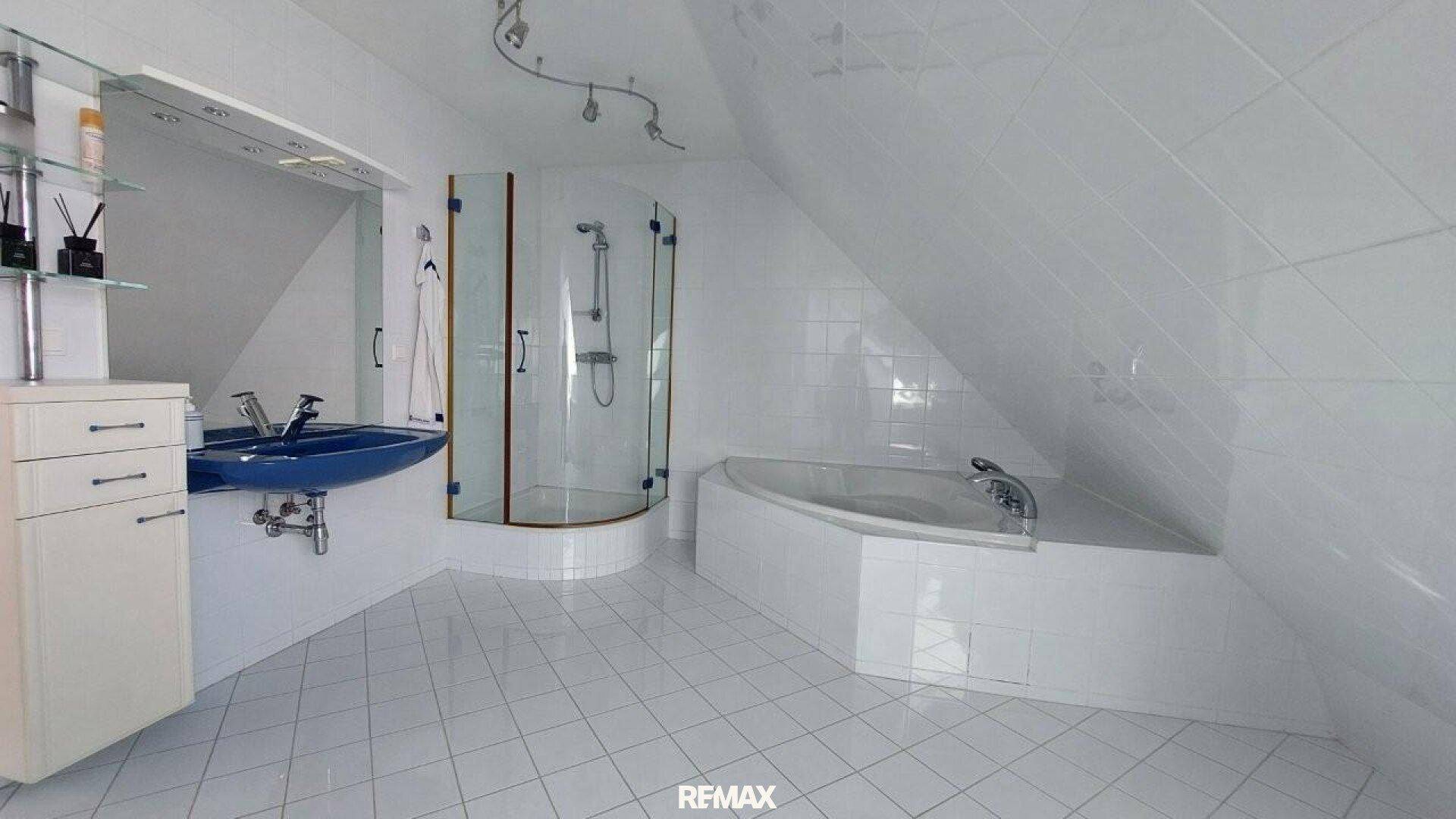 Geräumiges Badezimmer mit weiß gefliesten Wänden, Dusche und Badewanne unter Dachschräge.