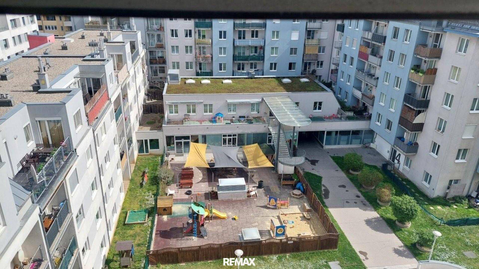 Luftaufnahme eines Gemeinschaftsspielplatzes mit Sonnensegeln und umliegenden Wohngebäuden.