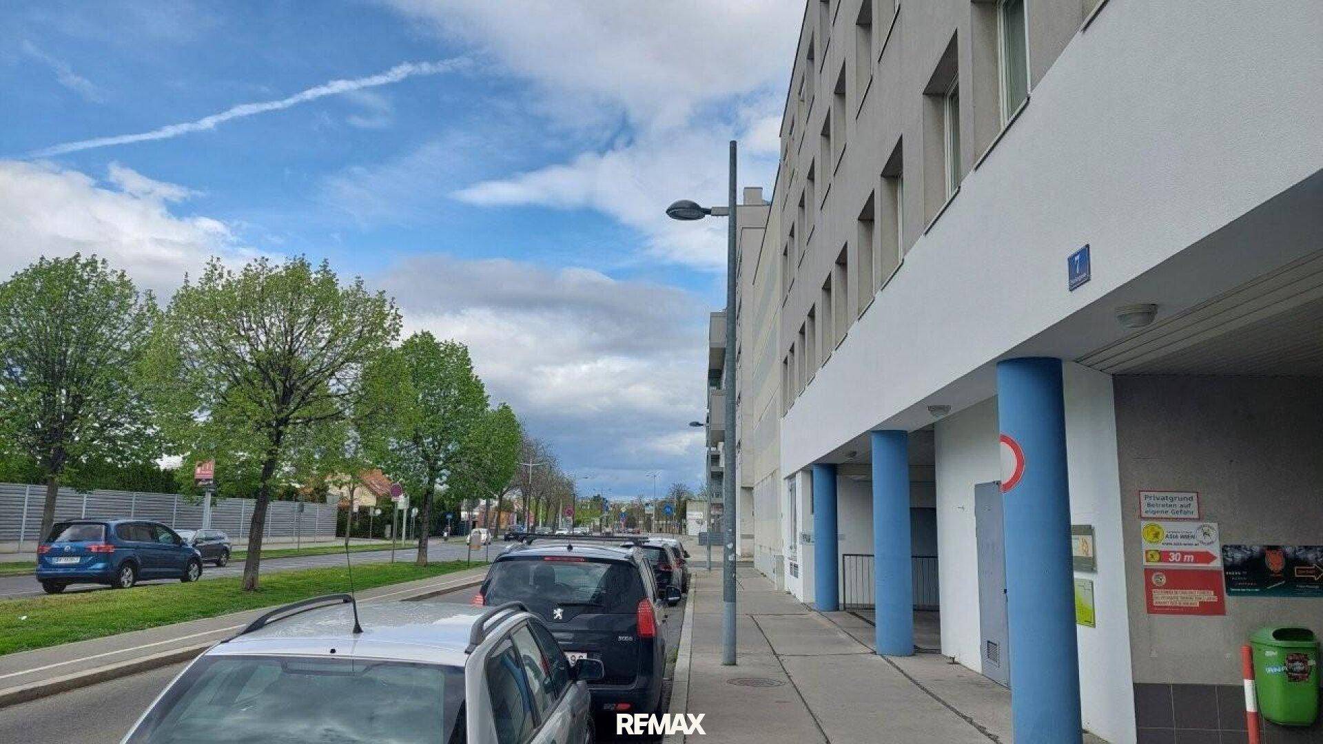 Straßenansicht mit parkenden Autos und einem modernen Wohngebäude mit blauen Säulen.