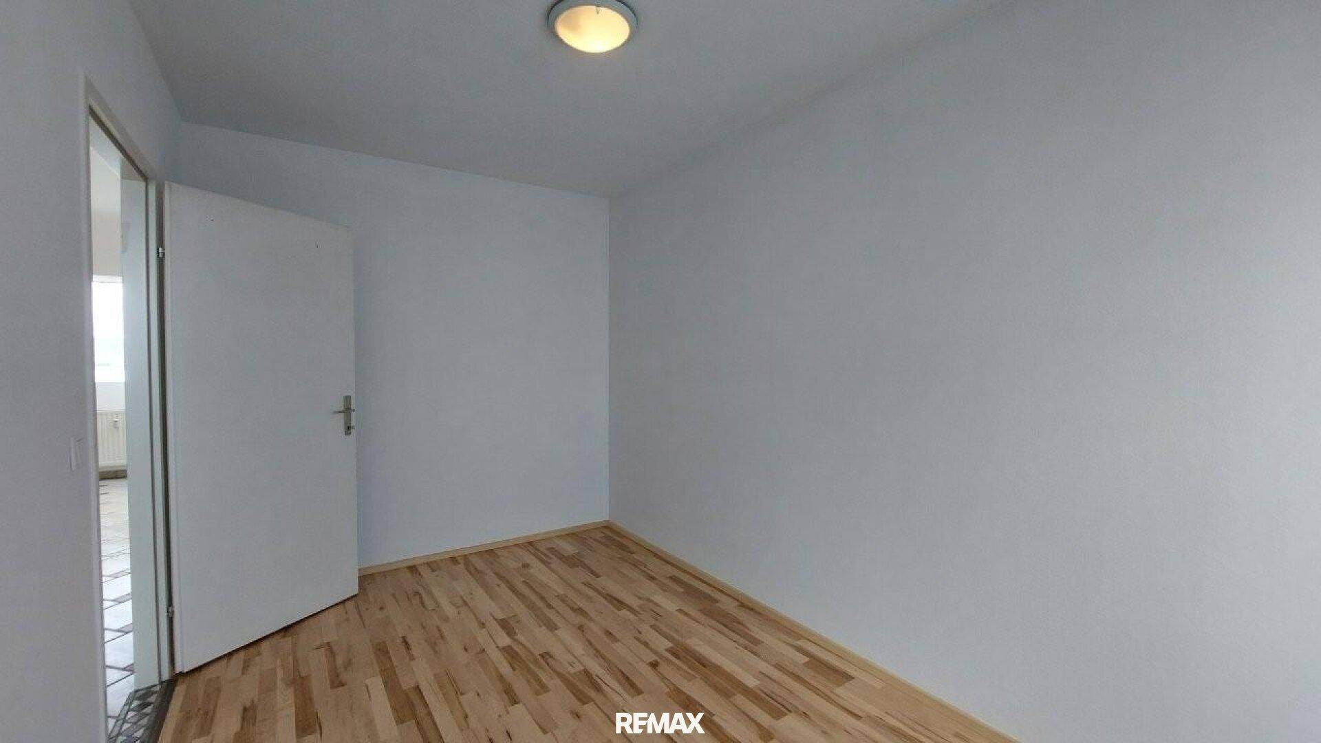 Helles Schlafzimmer mit Holzboden und weißen Wänden, bereit zur individuellen Gestaltung.