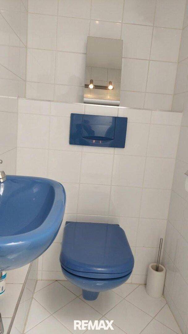Kleines WC mit blauem Waschbecken und Toilette, weiß gefliest.