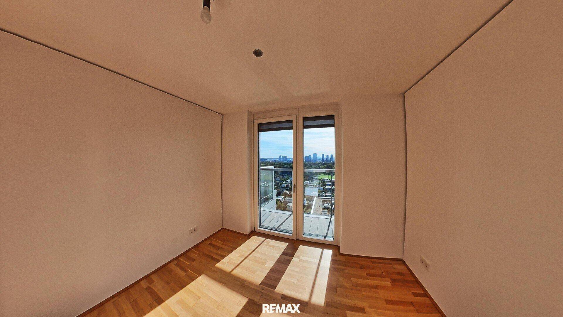 Helles Schlafzimmer mit Parkettboden, großen Fenstern und Zugang zu einem Balkon mit Stadtblick.
