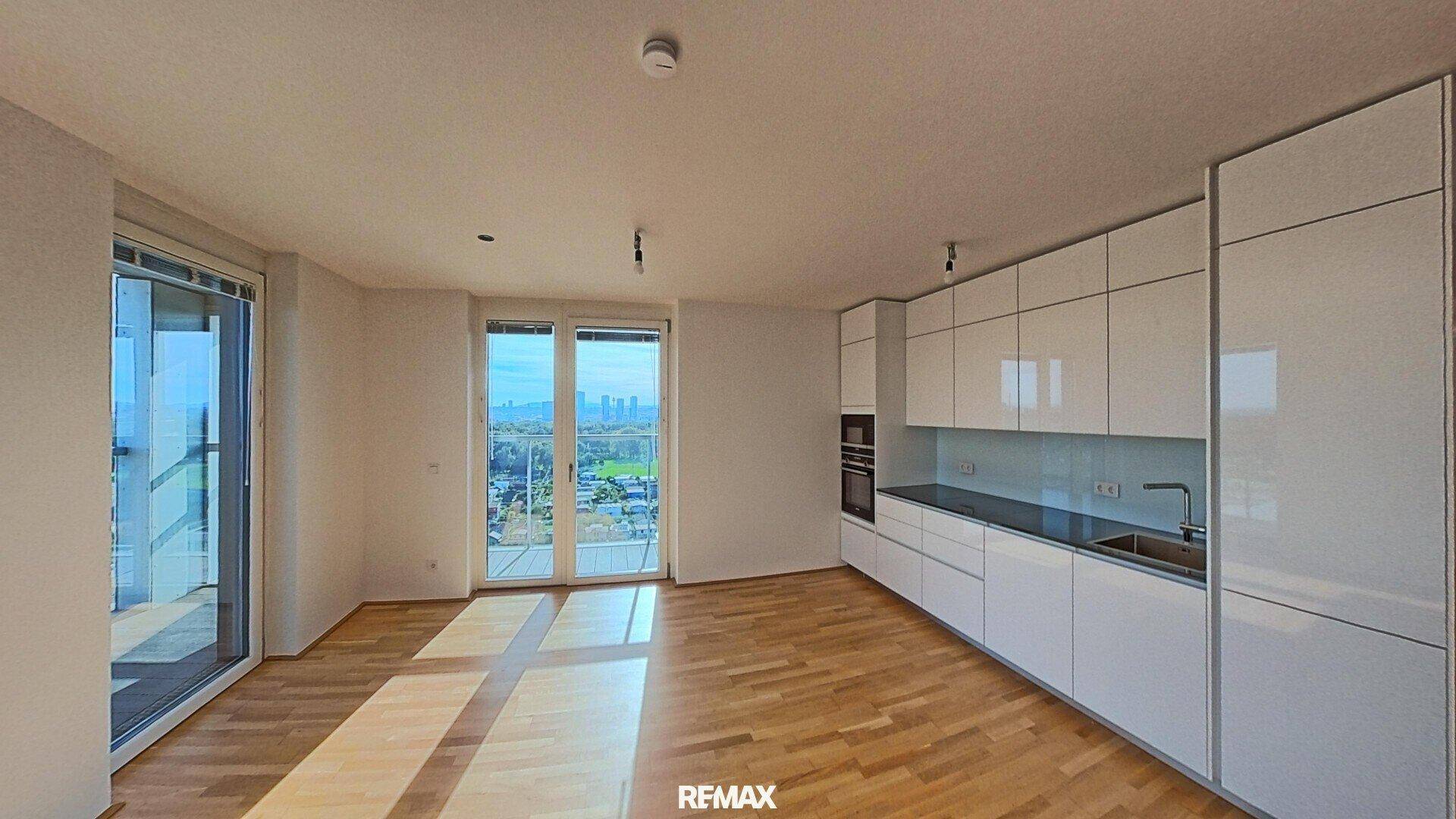 Lichtdurchfluteter Wohnbereich mit moderner weißer Einbauküche, Parkett und Zugang zum Balkon.