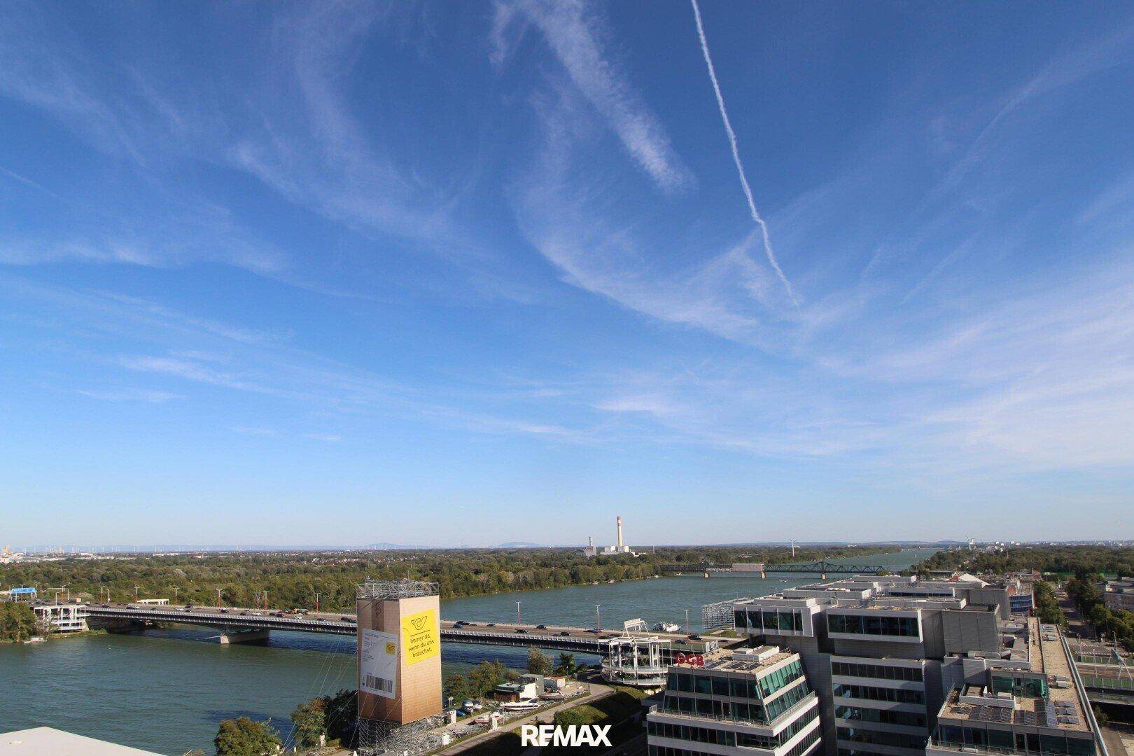 Weitläufiger Ausblick auf den Fluss, Brücken und die städtische Umgebung unter blauem Himmel.