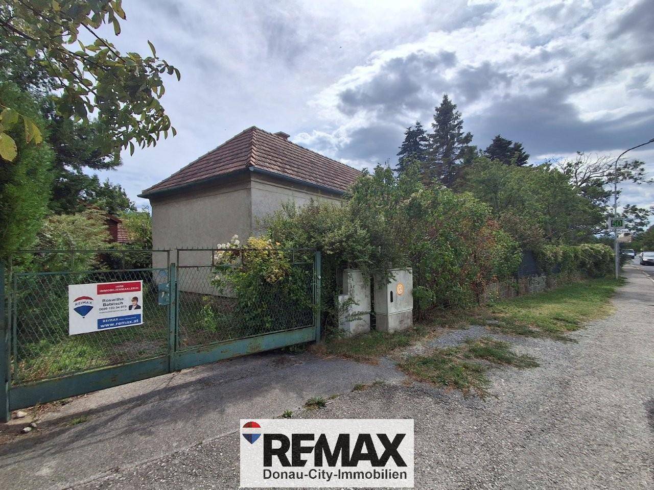 Vorderes Tor des Grundstücks mit einem Haus im Hintergrund und einer Straße daneben.