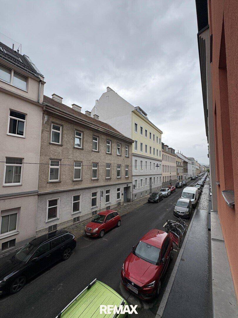 Lange Straße mit Gebäuden unterschiedlicher Bauart und parkenden Fahrzeugen.