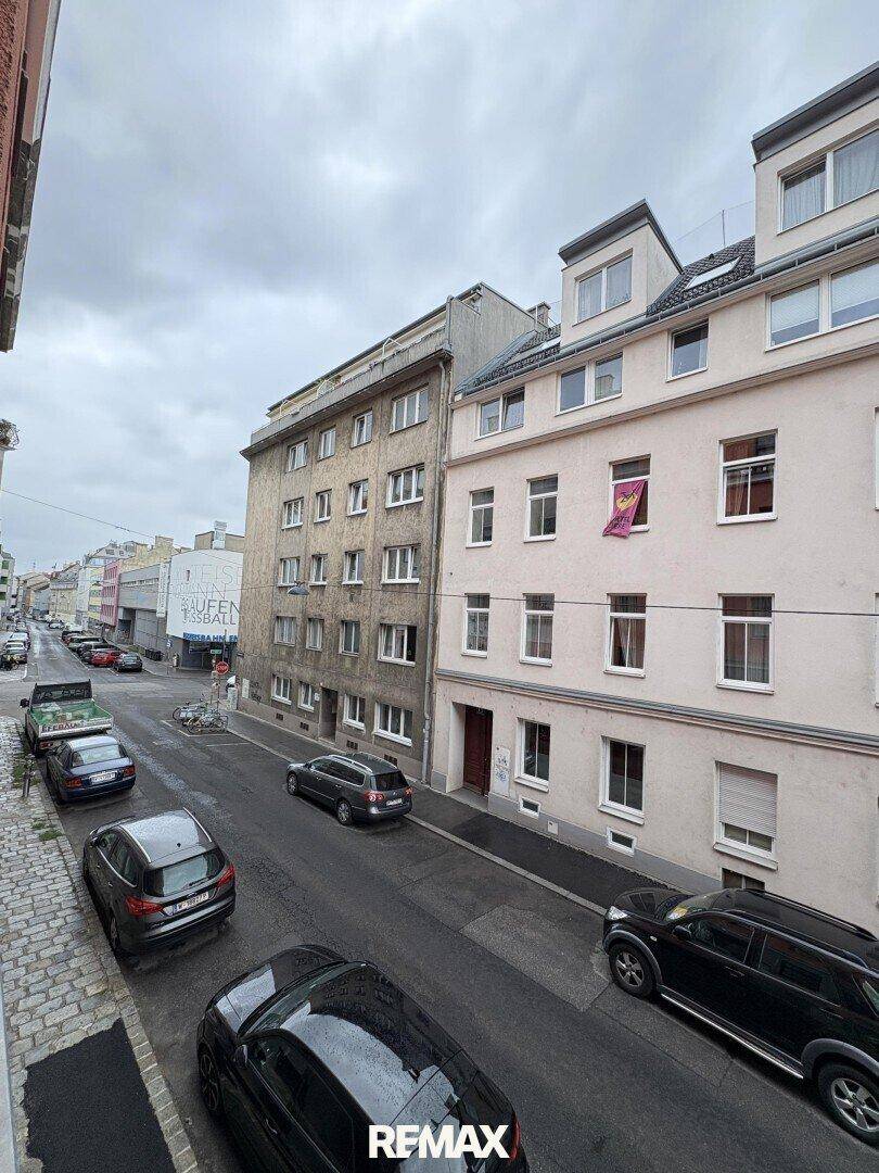 Blick auf eine belebte Straße mit parkenden Autos und angrenzenden Gebäuden.