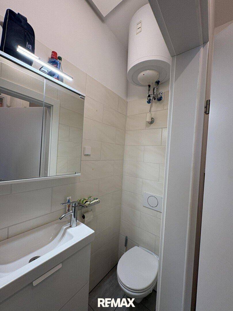 Kleines WC mit Waschbecken, Spiegel und Wandfliesen.