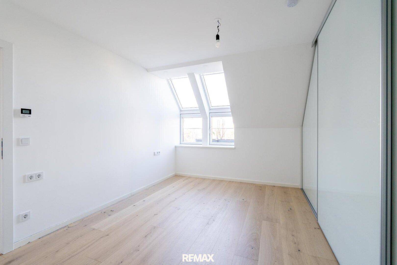 Helles Schlafzimmer mit Dachschrägen, großen Dachfenstern und hellem Parkettboden.